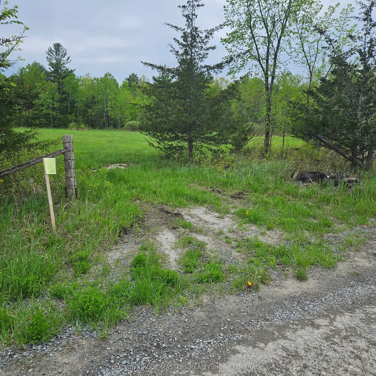 Aerial view of a vacant residential lot located between two existing homes, with road frontage, open grassy space, mature trees, and a private driveway beside a neighbouring estate-style home.
